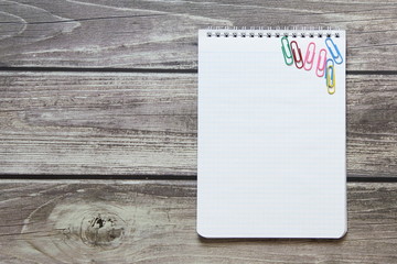 Notepad with a blank white sheet in a checker paper with paper clips lies on the background of wooden boards.