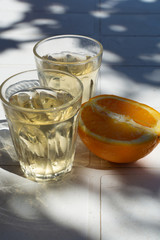 Greek wine in 2 glasses, fresh ripe orange served in garden in sun lights