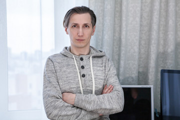 Fototapeta premium Portrait of handsome man dressed hoody, standing inside room with folded arms
