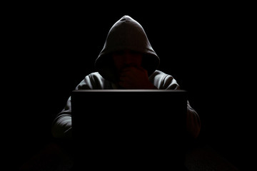 a computer hacker in front of a laptop put his hand to his face in the dark