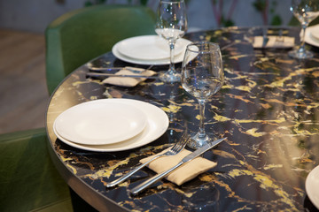 Fototapeta premium Top view copy space . Round marble table. Green chair. Set of cutlery knife, spoon, fork, plate, wine glass. Black marble table .