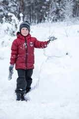 Fototapeta na wymiar Caucasian boy in red jacket standing near snowman in forest