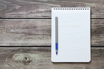 Notepad with a blank white sheet in a checker paper with ball pen lies on the background of wooden boards