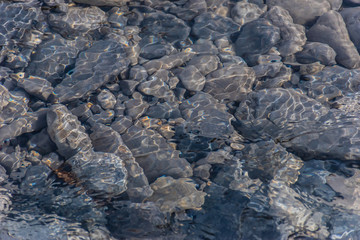 Pebble under clean transparent water of a mountain river with sunlight reflecting and flickering...