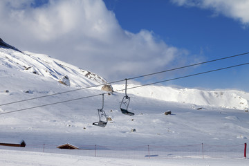 Snowy slope, ski-lift and blue sky with clouds at sunny winter evening