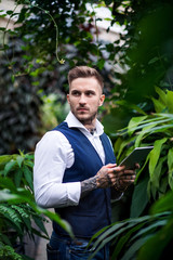 Young man with tablet standing in botanical garden.
