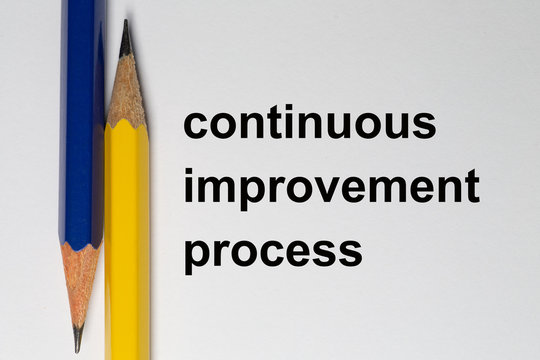Two sharpened pencils point in opposite directions and are placed vertically on a white background. The solgan continuous improvement process is written in black on the background