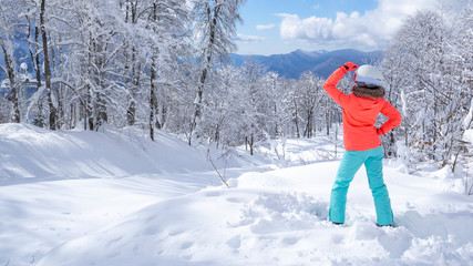 Young female skier in bright jacket stands and looks at the scenic mountain landscape. The concept of sport and recreation. space for text, back view