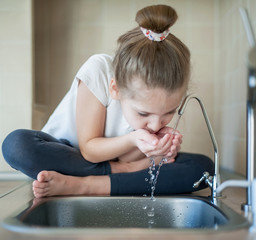 Caucasian little girl drinking from water tap or faucet in kitchen. Hands open for drinking tap water. Pouring fresh healthy drink. Good habit. Right choice. Environment concept. World Water Day.