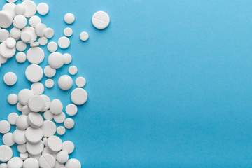 scattered white pills on a blue table. Layout for special offers such as advertising or other ideas. The concept of medicine, pharmacy and healthcare. Space for copy. flat lay for text or logo.