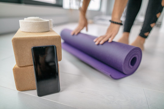 Phone app screen closeup at fitness yoga studio in indoor gym or at home. Girl rolling out mat getting ready for fit exercise workout with mobile smartphone showing online class.