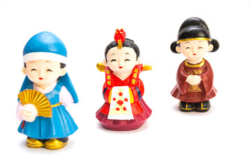 Three decorative ceramic Korean figures, two women and man, standing one by one in traditional colorful clothes Han bock isolated over a white background. Focus on the woman in red dress
