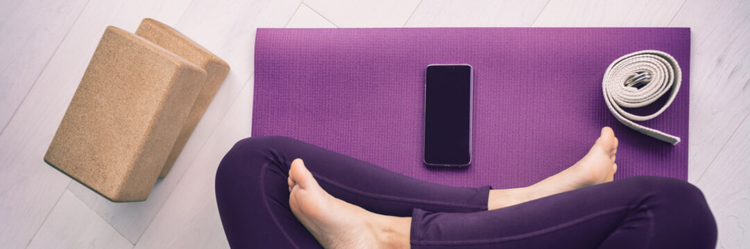 Yoga woman using mobile phone panoramic banner top view of cellphone on exercise mat and blocks, stretching strap.