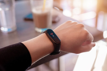 Girl measures her heart rate with a smart bracelet. Close-up. Coffee shop in background
