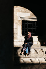 Photo of beautiful woman with hijab sitting at stairs of old historical building in Dubrovnik, Croatia. 