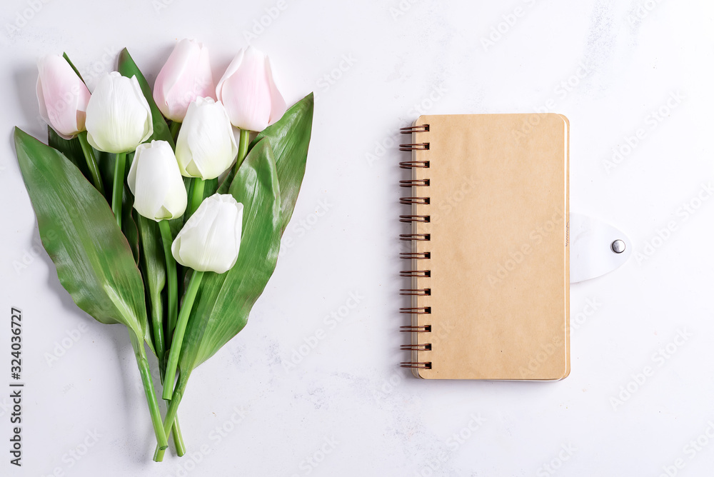 Wall mural Pastel Tulips with notebook on white marble background, copy space