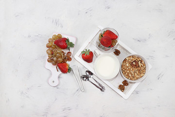 Obraz na płótnie Canvas Granola with yogurt and fresh strawberries and grapes on a light table. The concept of healthy and natural food, diet useful dessert in a glass. Healthy breakfast, food for children
