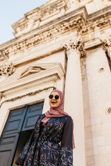 Fototapeta premium Portrait of beautiful woman with hijab standing in front of old church, historical building, in Dubrovnik, Croatia. 