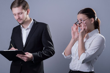 Portrait of a pair of young people of twenty-five years.in business clothes. A businessman with a serious looks at a folder of papers next to a young girl subordinate trying to seduce the boss.