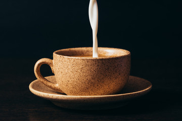 Milk is pouring into a cup of coffee on a black background.