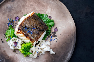 Gourmet gebratenes Skrei Kabeljau Fisch Filet mit Broccoletto Rapa und Nudeln als Draufsicht auf einem Modern Design Teller mit Textfreiraum rechts