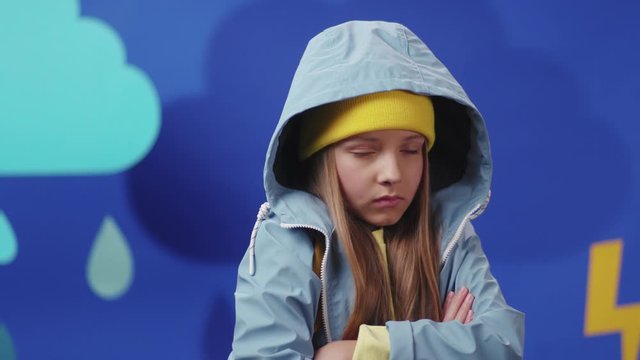 Unhappy beautiful teenager is staying under heavy rin thunderstorm getting cold and wet isolated on blue background. Weather conditions.