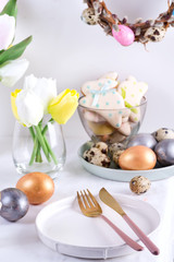 Easter table setting with tulips, easter eggs, cookies and plate with cutlery on white table