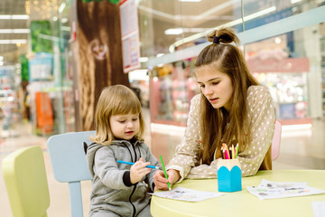 Adorable girl draw on plastic tablet in shop.Two girls decorate a children's drawing in a shopping center, waiting for their parents with purchases. entertainment for children.
