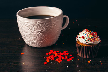 Cup of coffee with heart-sprinkled cupcake.