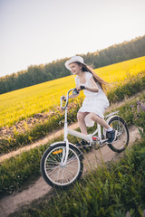 Fototapeta premium Cute girl in a white dress rides a bicycle on a field with flowers