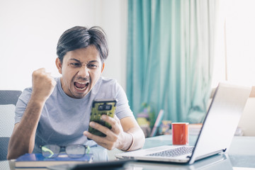 Good news,Young Asian office worker receiving great news over his smartphone