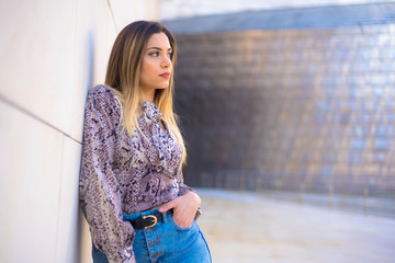 An elegant young blonde with high heels, a shirt and a short denim skirt in a Street Style session. Thoughtful look