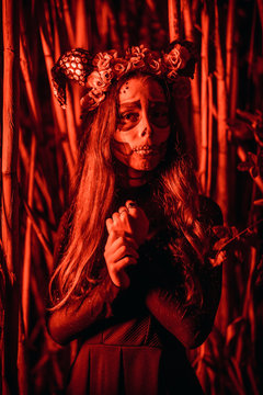 Halloween, a young girl dressed as a Mexican skull among bamboos in a black dress, with red lighting