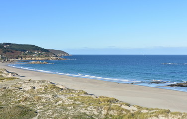Beach with promenade, sand dunes with grass and blue sky. Arteixo, Coruña, Galicia, Spain.
