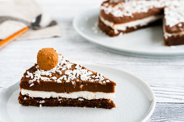 piece of chocolate cake on a plate. Chocolate and coconut cake on a white wooden background. Foodfoto in a high key. Raw dessert