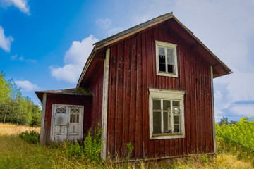 old Finnish abandoned haunted house on a background of blue sky and green tarva not far from...