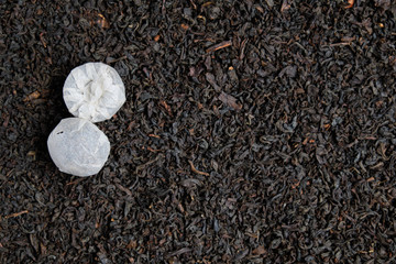 Round bundles of tea on a background of dry scattered black tea. Copy space. Top view.