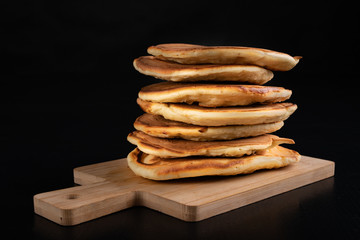 Pile of fresh pancakes on a wooden board. Tasty cookies on the kitchen table.