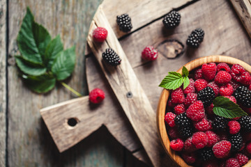 raspberries and blackberries on a wooden background in vintage style. Cutting board