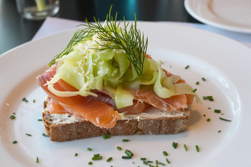 whole grain bread with salmon, cucumber, horseradish flakes and dill garnish served on a white plate