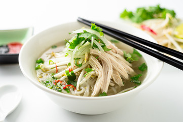 Vietnamese pho noodle soup bowl closeup. A classic authentic vietnamese food, this pho soup is served in a white bowl with chicken broth and lots of fresh garnishes such as cilantro and bean sprouts.