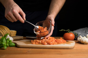 Person preparing Italian bruschetta diced tomatoes on wooden board dark background