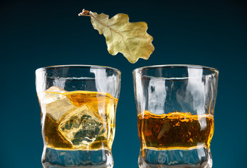 Two glasses of whiskey, ice and a dry oak leaf