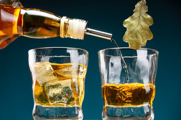Whiskey is pouring from a bottle into a glass. A glass of whiskey with ice.