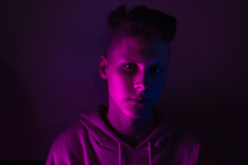 Young guy in a neon light. A teenager in a pink hoodie in trendy lighting of pink, purple and blue