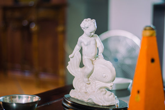 escultura de yeso de un angel en cima de un pez, blanco con fondo borroso color azul, decoraci&oacute;n para el interior de la casa