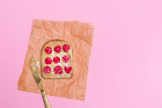 Peanut butter toast with raspberries on pastel pink background. Image with copy space, top view