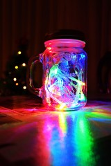 Glass jar with colored lights and Christmas pine in the background