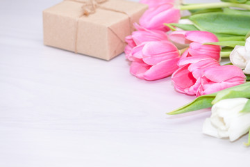 Craft present or gift box with tulips on white wooden background. Flat lay, copy space. Spring, holiday, mother's, women's day concept.