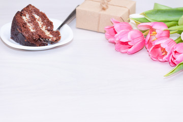 Bouquet of pink tulips, chocolate cake. pressent box on white wooden background. Copy space, close up. Mother's, women's day concept.